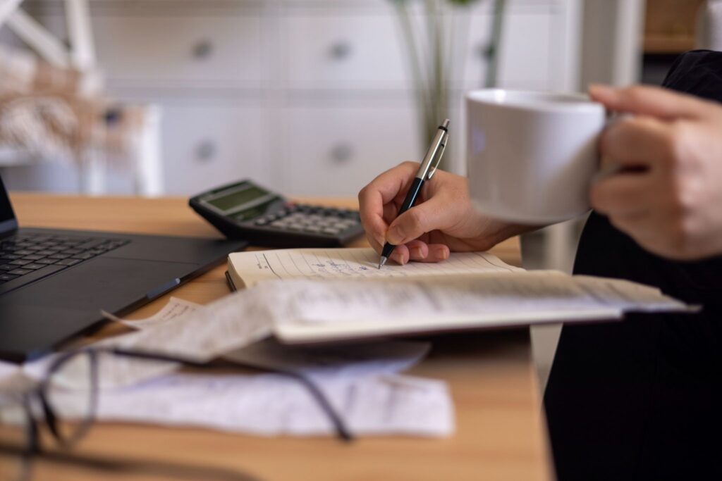 A stressed homeowner reviewing complicated financing papers and monthly statements at a wooden desk with a laptop open.
